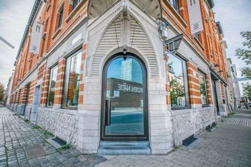 Immeuble d'angle avec entrée vitrée, façade en briques et en pierres, et rue pavée.