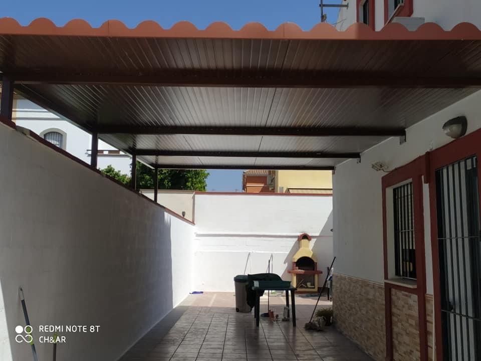 Área de patio cubierto con techo marrón, paredes blancas y piso de baldosas.