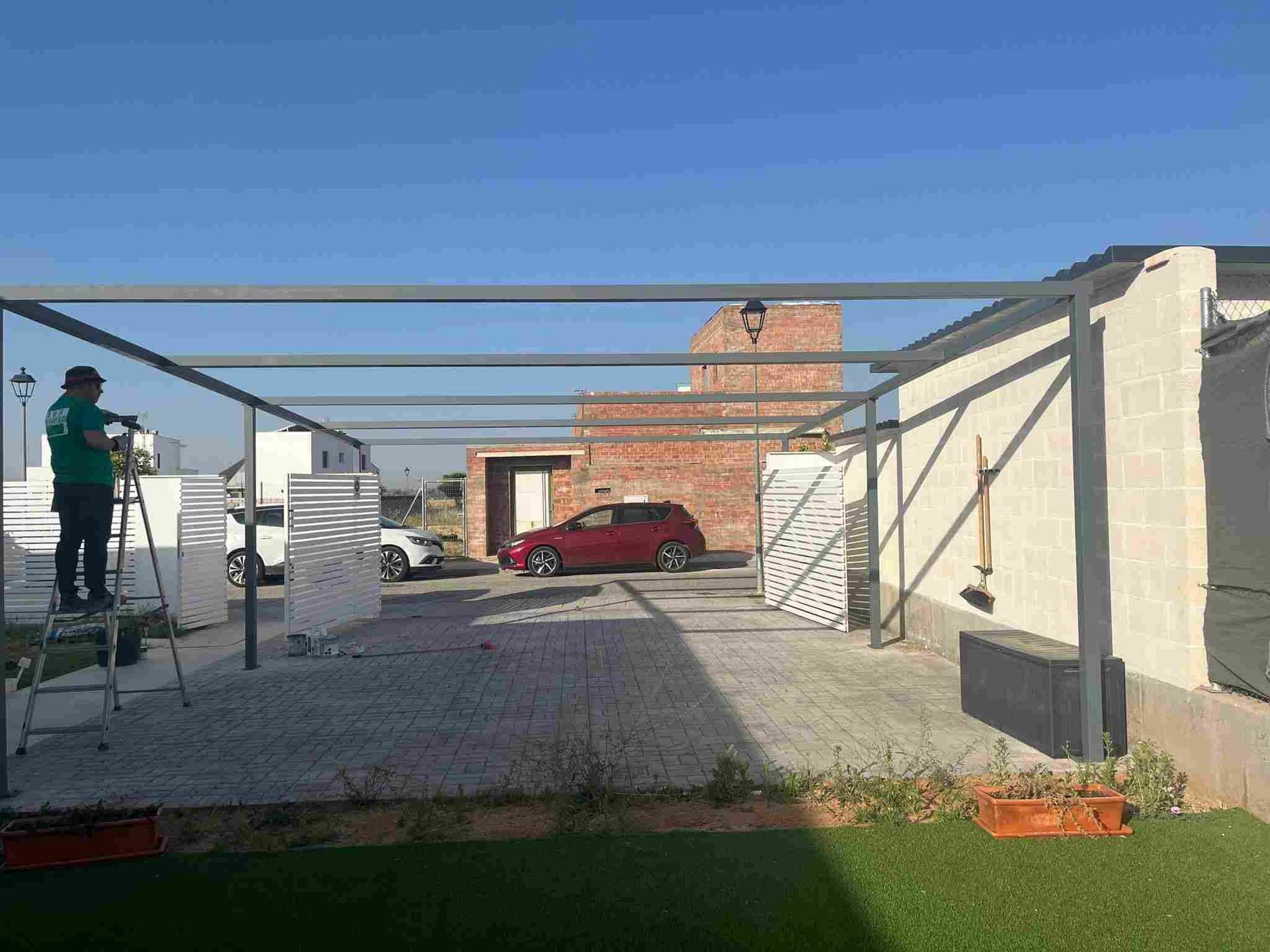 Una persona trabaja en una estructura de metal al aire libre; hay un coche rojo aparcado cerca.