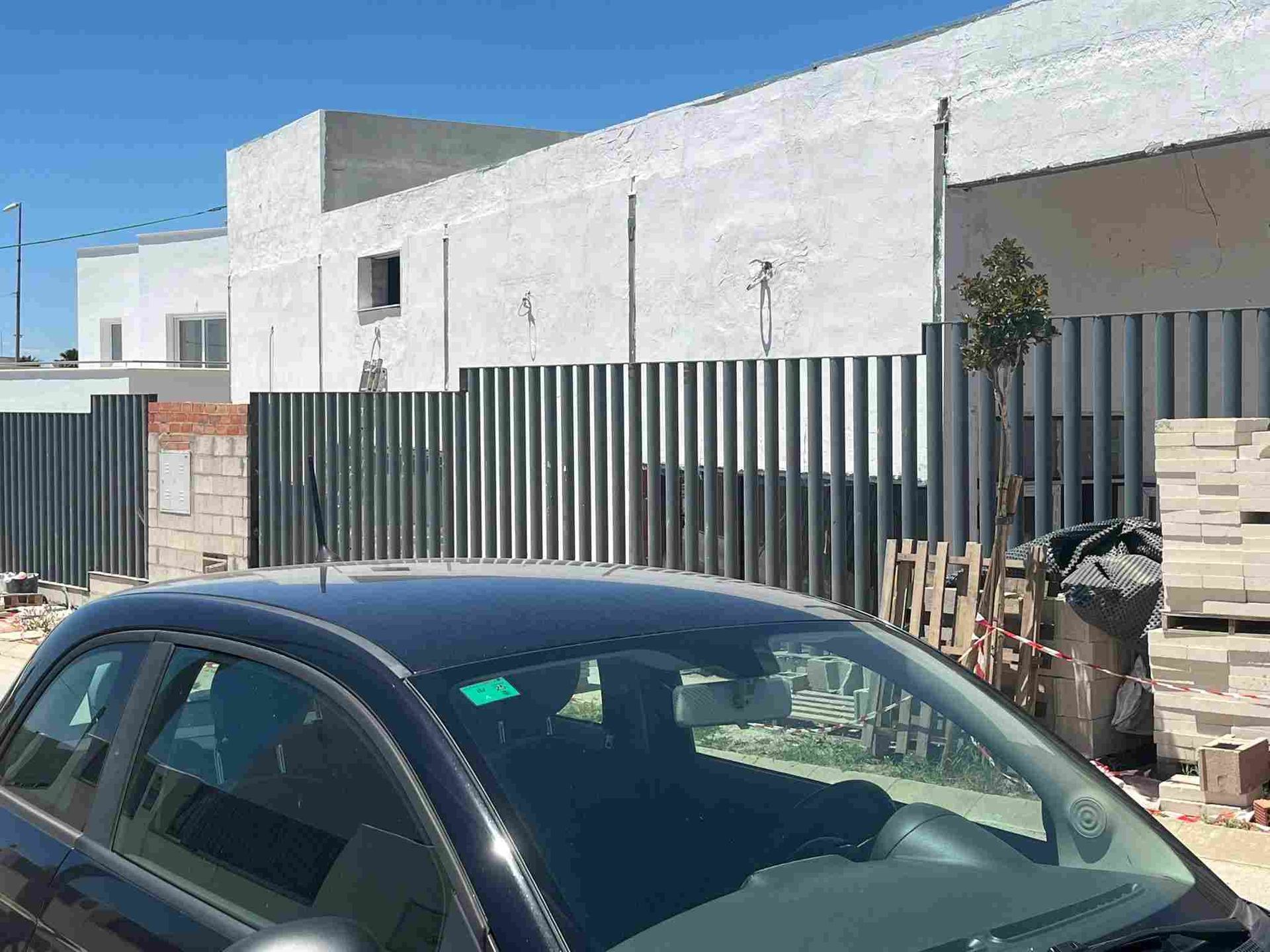 Un coche negro delante de un edificio con valla metálica. Un día soleado y brillante.