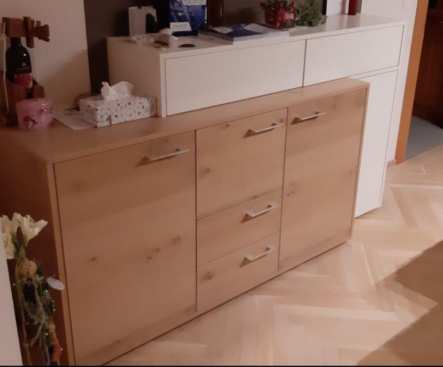 Anrichte aus Holz mit Schubladen und Türen, darauf ein weißer Schrank.