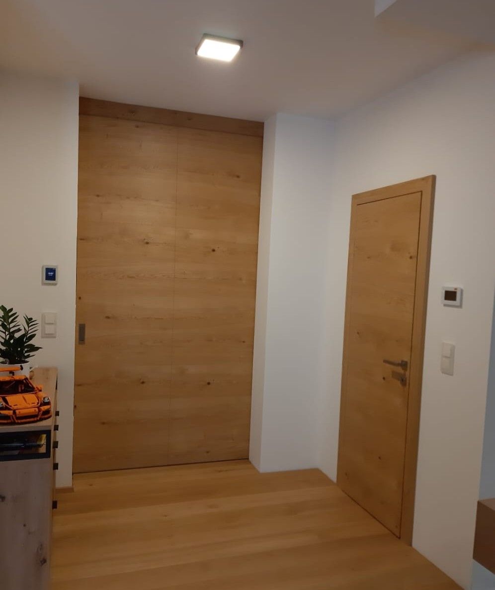 Holztüren in einem Flur. Eine große, eine normale. Heller Holzboden und weiße Wände.