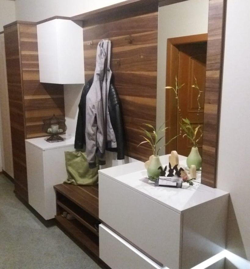 Eingangsbereich mit holzgetäfelter Wand, weißen und braunen Schränken, Garderobe, Spiegel und Dekorationselementen.