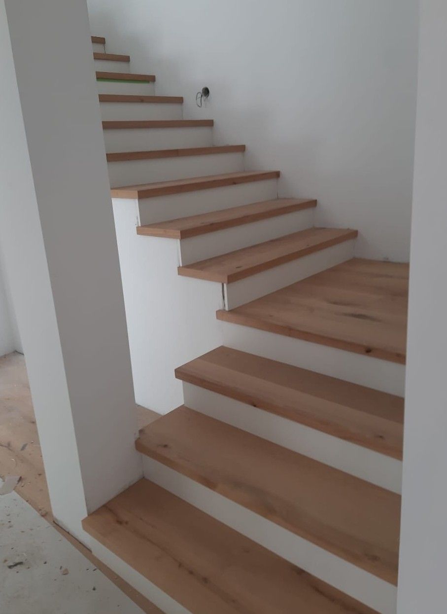 Holztreppe mit weißen Setzstufen vor weißen Wänden.