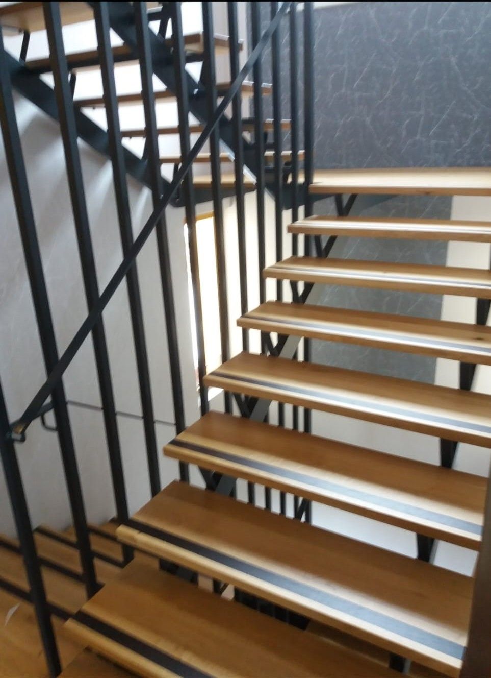 Holztreppe mit schwarzem Metallgeländer. Sicherheitsstreifen an den Stufen.