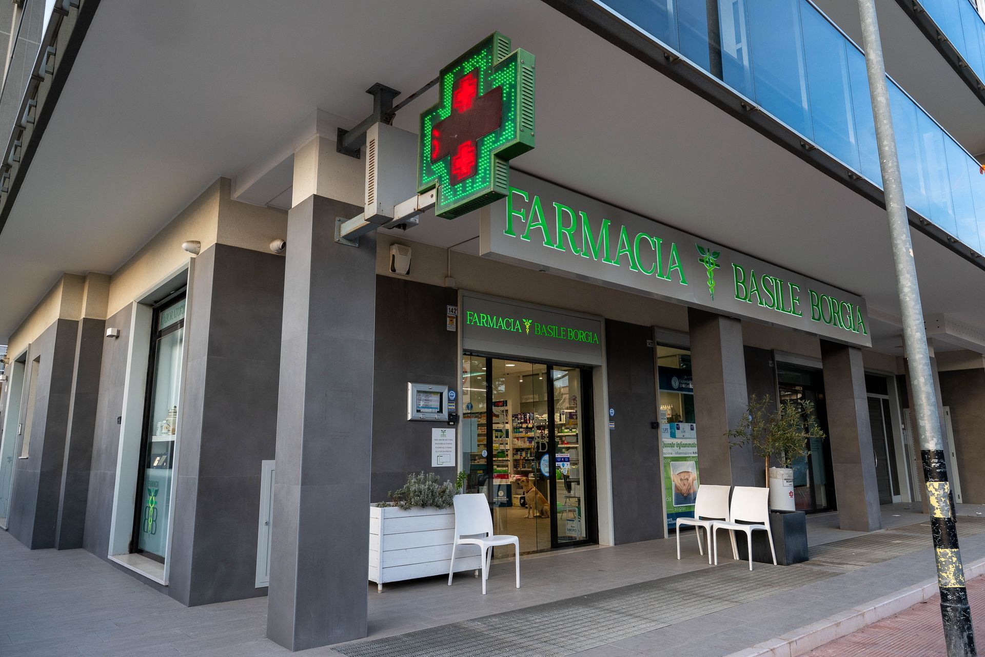 Esterno della farmacia Basile con ingresso sotto ai portici e croce illuminata