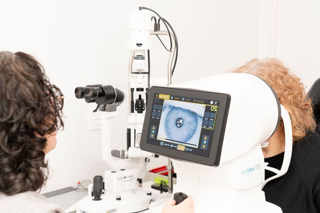 Un médico utilizando un aparato para examinar los ojos, con un monitor que muestra un primer plano de un ojo.