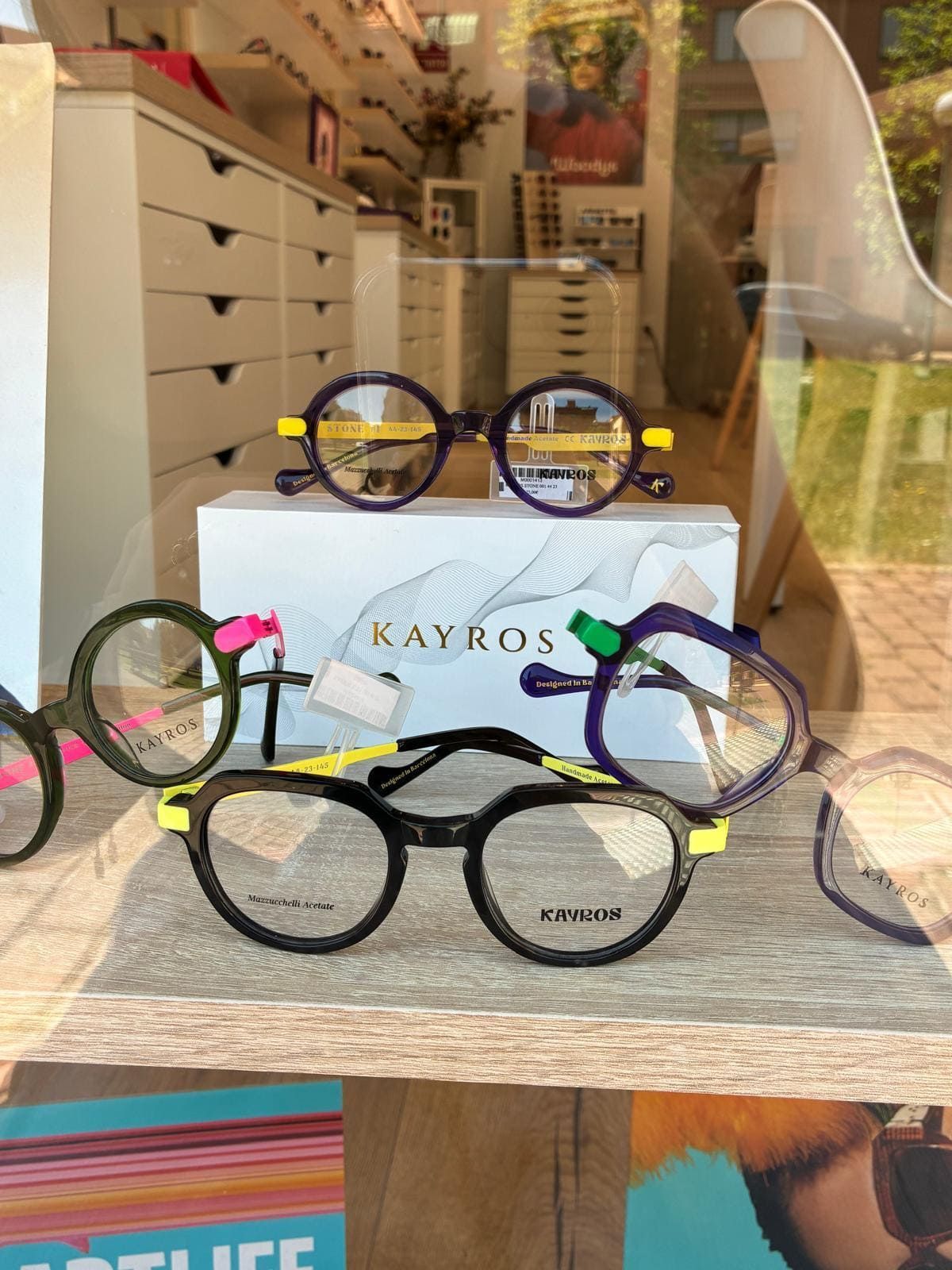 Cuatro monturas redondas de gafas sobre una mesa en el escaparate de una tienda, con una caja con la etiqueta “KAYKO” detrás.