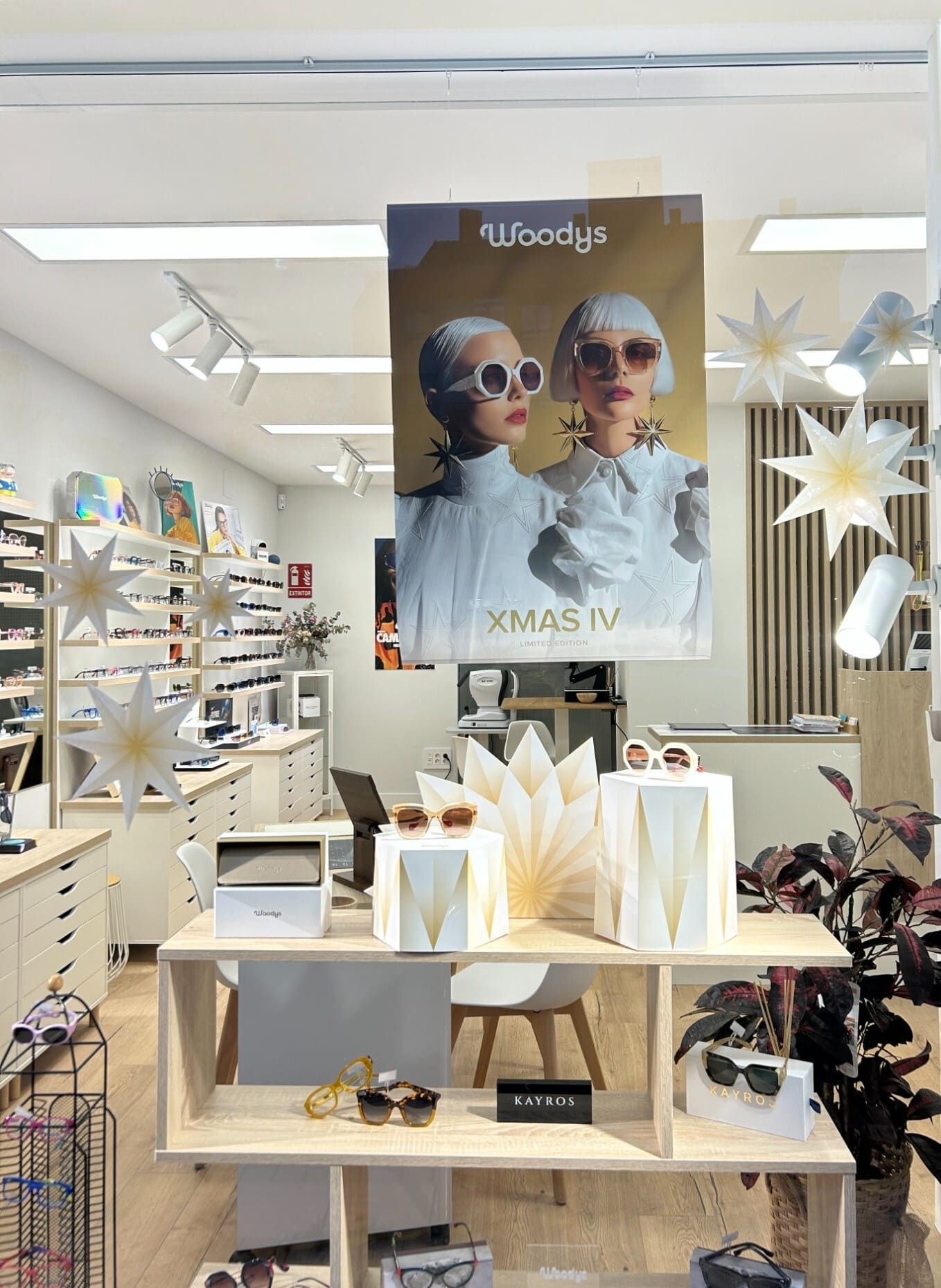 Escaparate de tienda con adornos navideños blancos y dorados, estanterías y un gran cartel promocional.