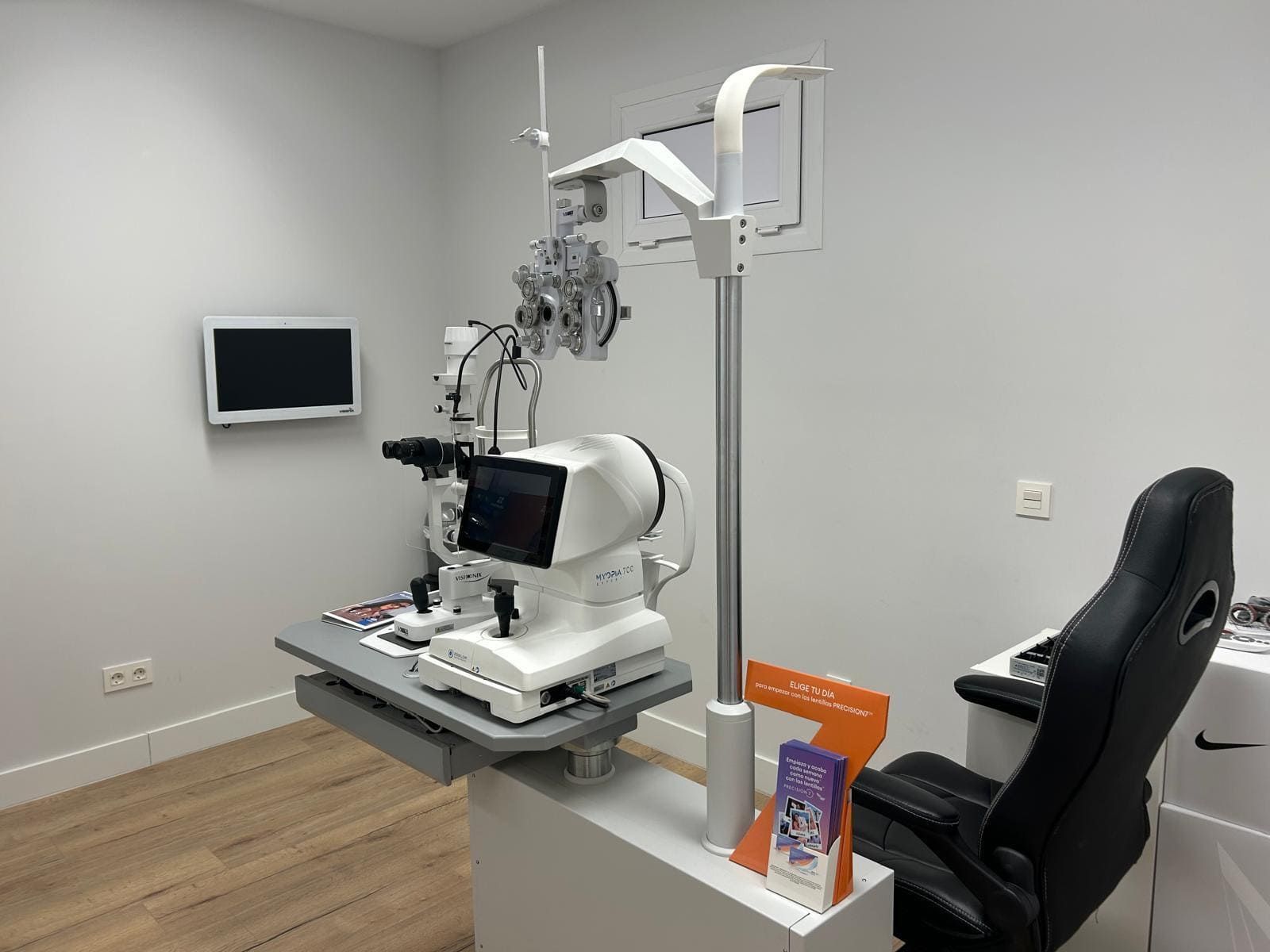 Sala de examen médico con una lámpara de hendidura para examinar los ojos, un monitor y una silla negra