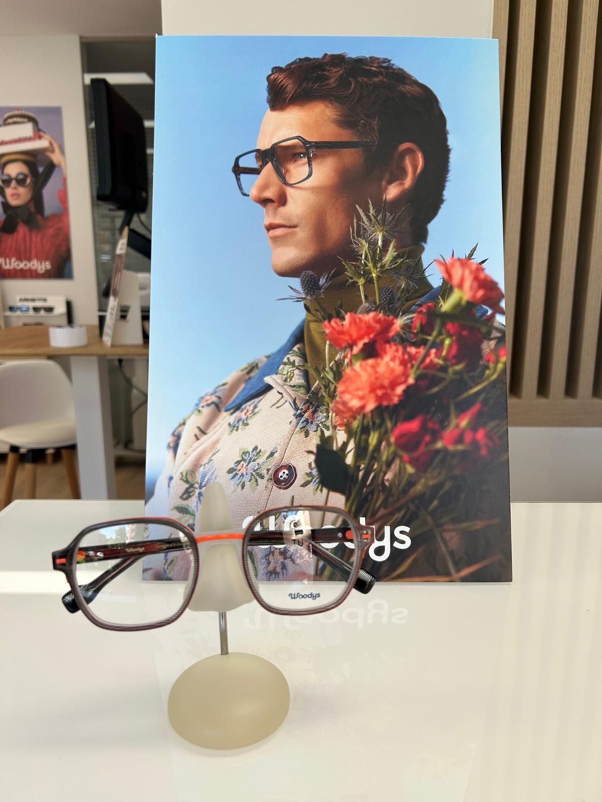 Gafas expuestas delante de un póster con el retrato de un hombre, flores y un fondo azul