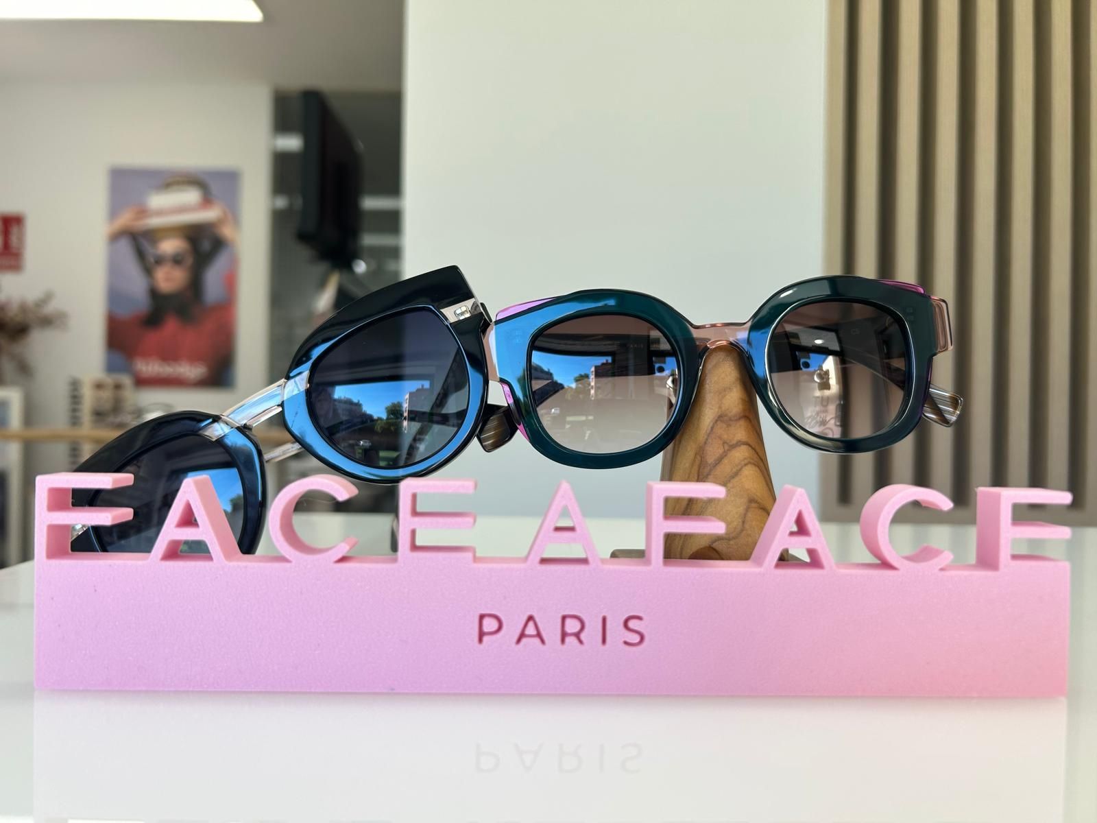 Expositor rosa de FACE A FACE con gafas de sol sobre un estante blanco, en el escaparate de una tienda