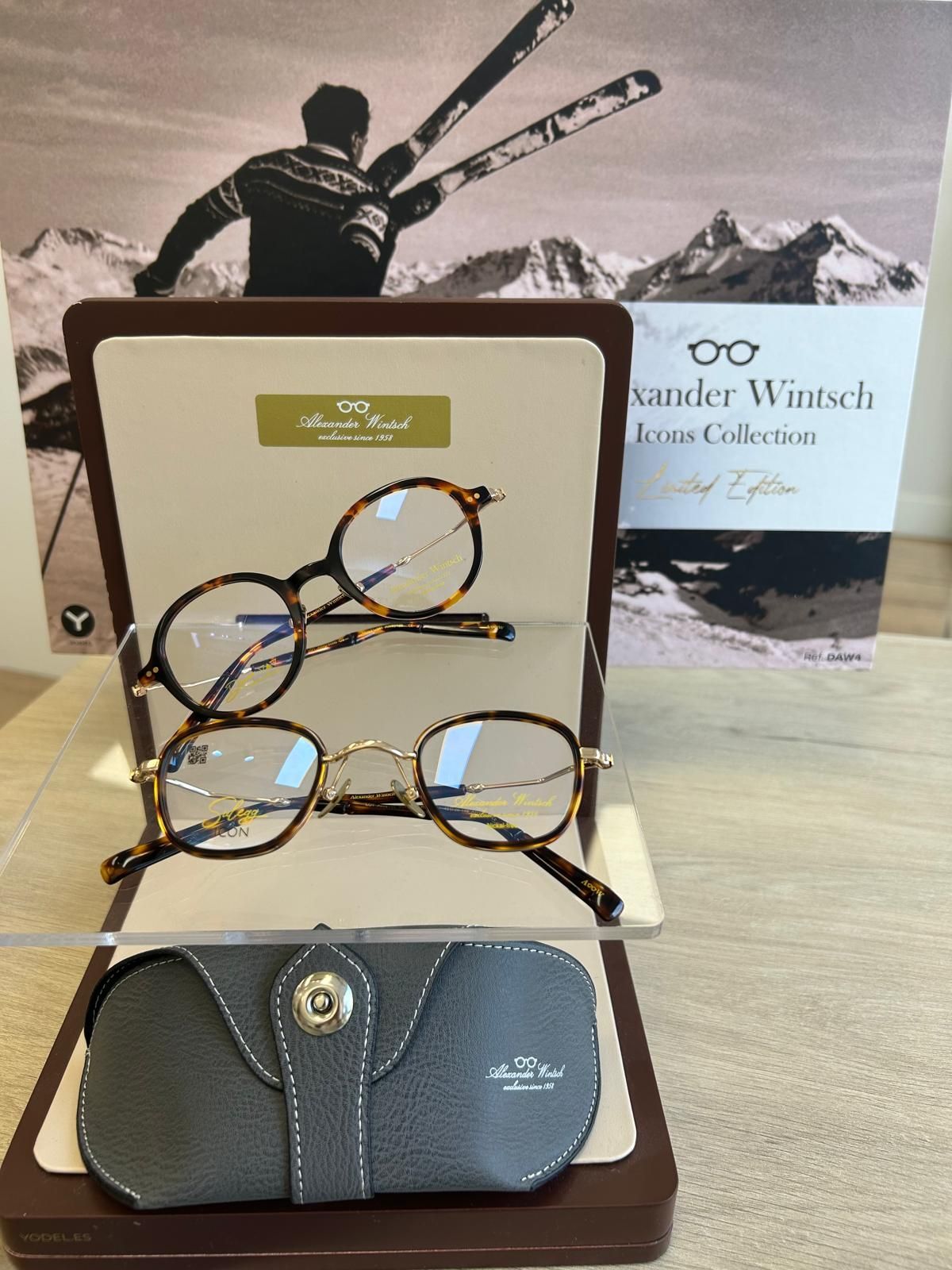 Tres pares de gafas sobre un expositor, con un estuche gris delante y una caja de producto de fondo.