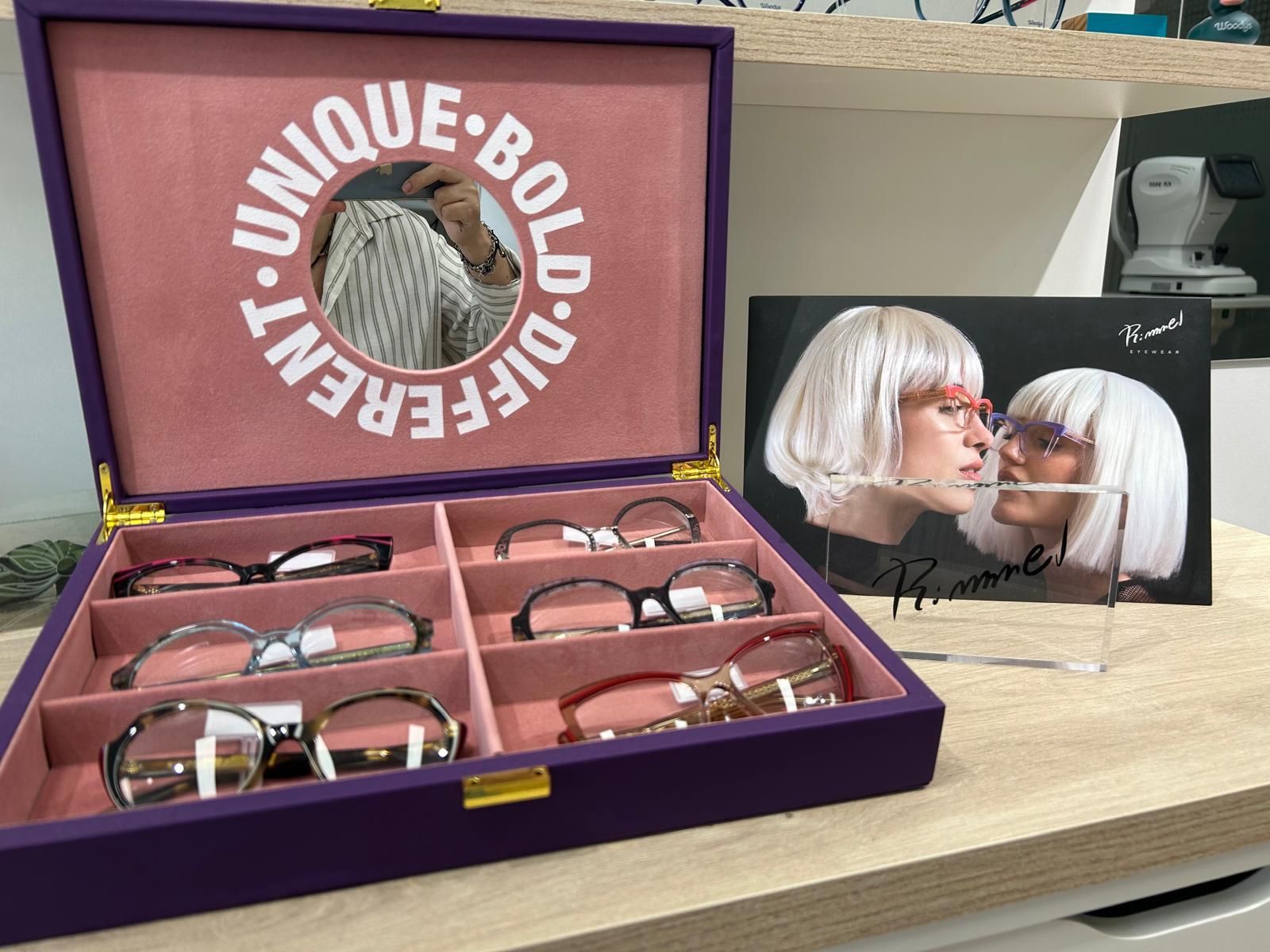 Estuche morado para gafas con cuatro pares de gafas y una tarjeta publicitaria a juego sobre un escritorio.