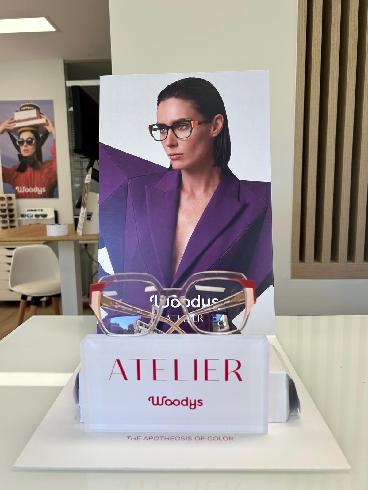 Una tarjeta morada de exposición de moda sobre una base blanca que dice «ATELIER» y «Woodys» en una sala de exposición.