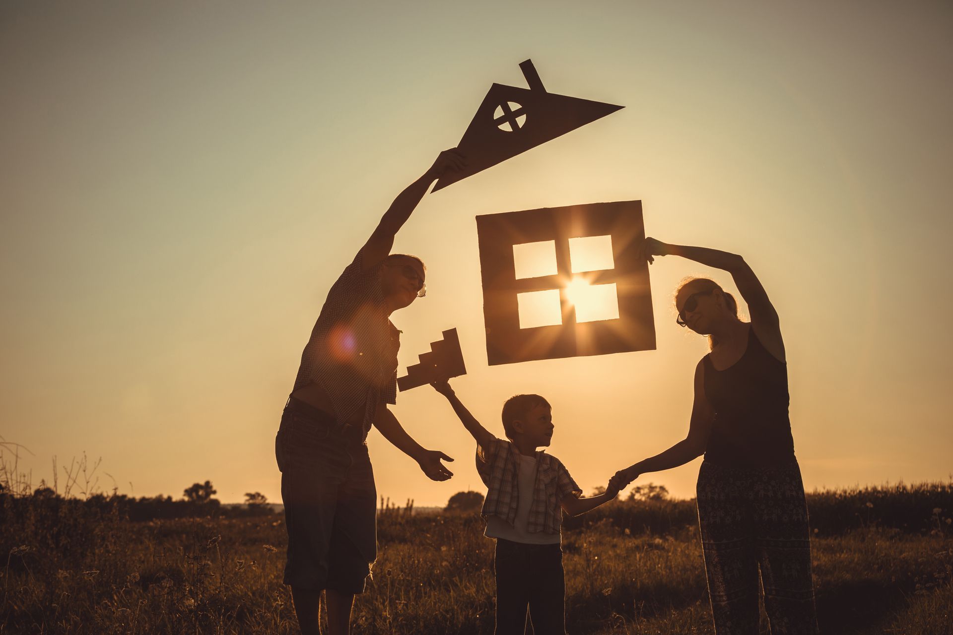 La silhouette d'une famille, découpée en formes de toit et de fenêtre, se détache sur un coucher de soleil, dessinant ainsi la silhouette d'une maison.