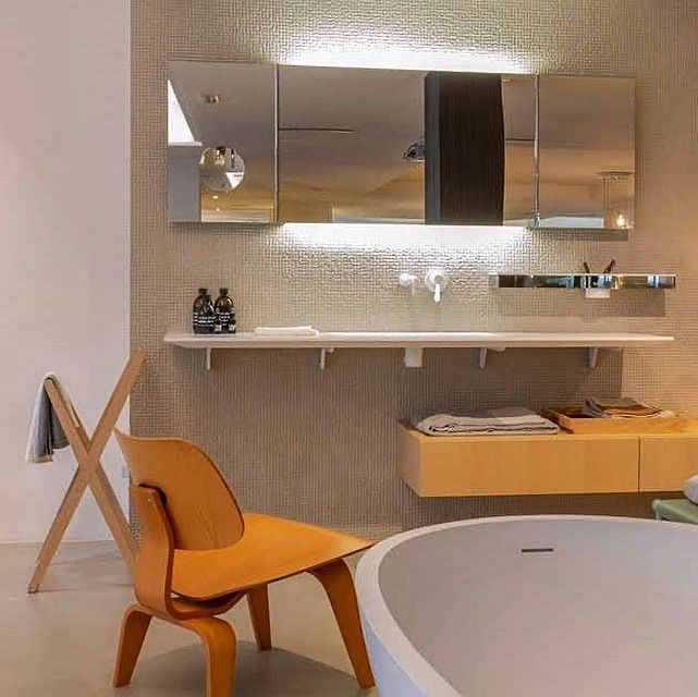 Un baño con bañera, lavabo, espejos y una silla.