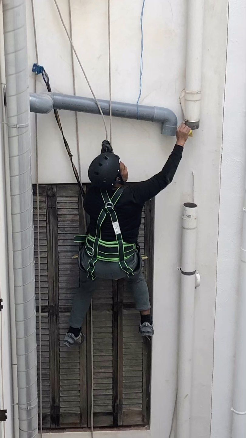 Un hombre está pintando una tubería en el costado de un edificio.