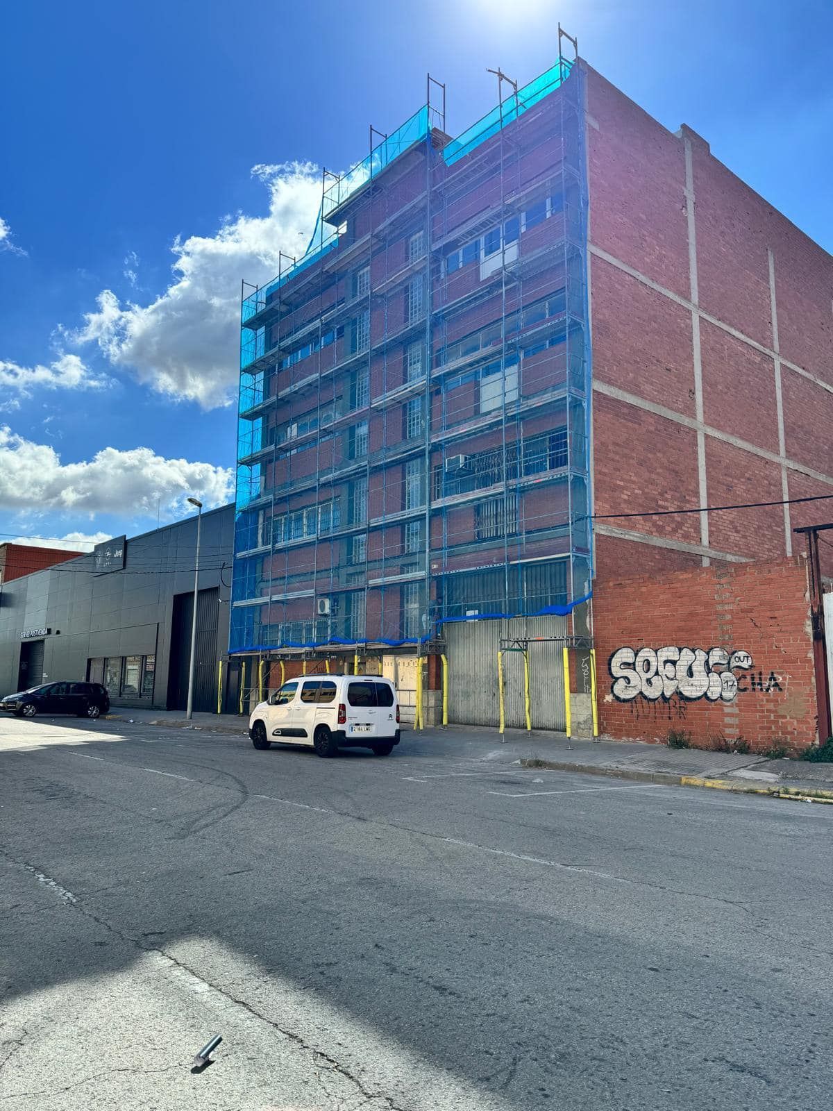 Una camioneta blanca está estacionada frente a un gran edificio de ladrillo cubierto de andamios.