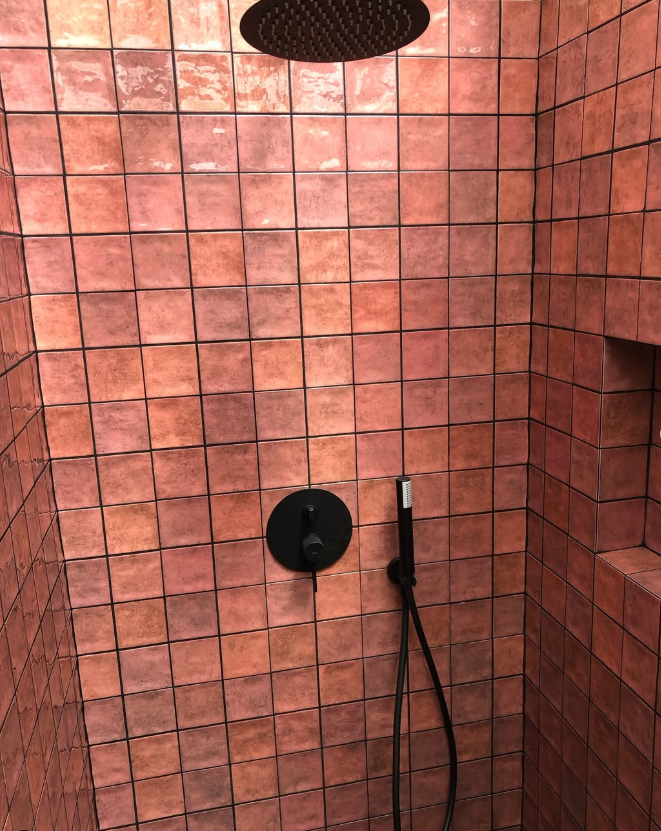 Una ducha con azulejos rojos y un cabezal de ducha negro