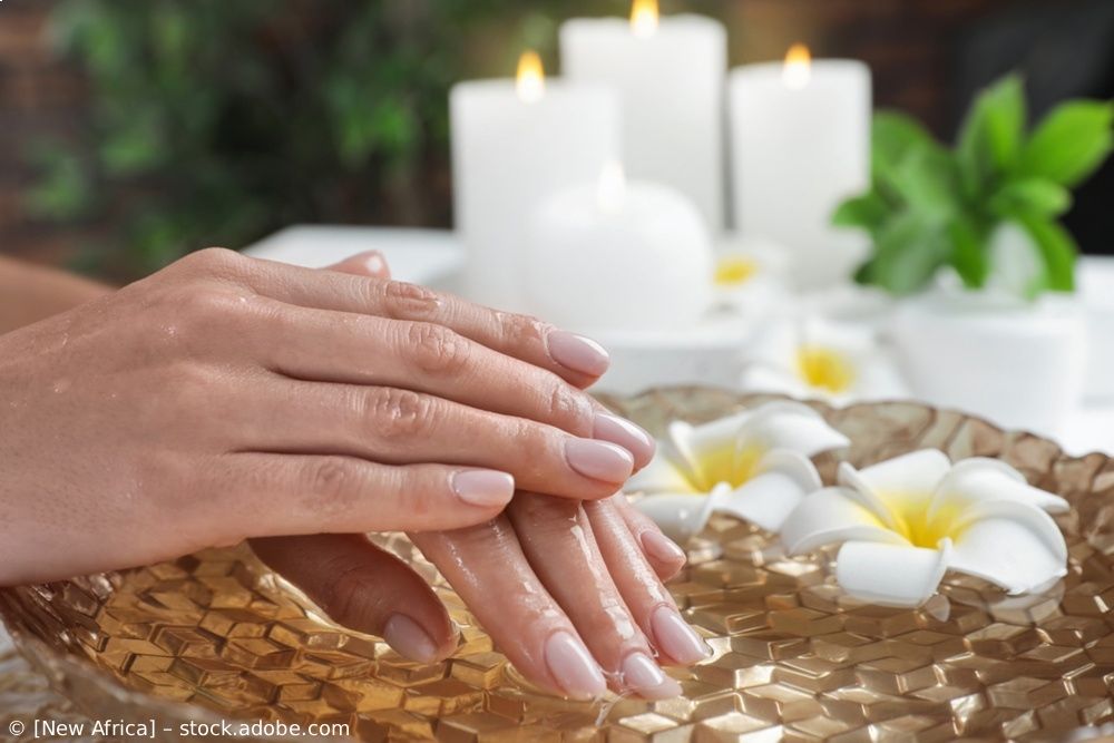 Hände bei einer Spa-Handmassage mit weißen Blumen und brennenden Kerzen auf einem geflochtenen Tablett