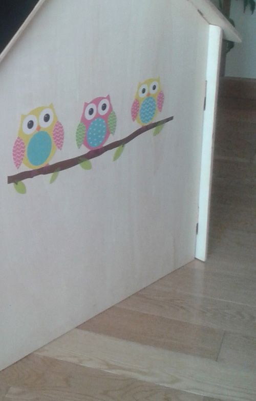 Tres búhos están sentados en una rama sobre una pared blanca.