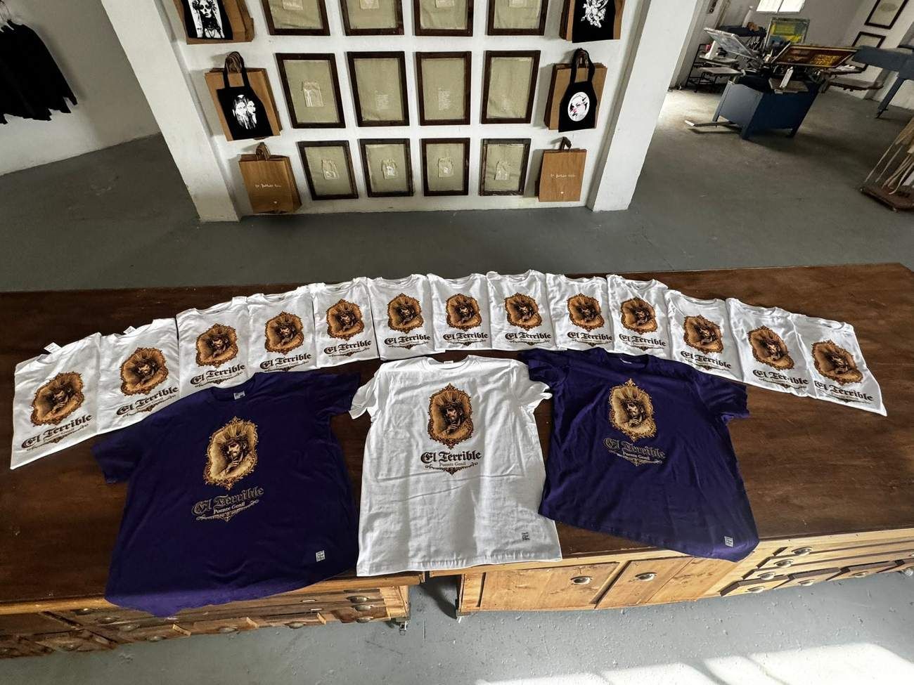Camisetas y estampados expuestos sobre una mesa en un puesto de una tienda o mercado.