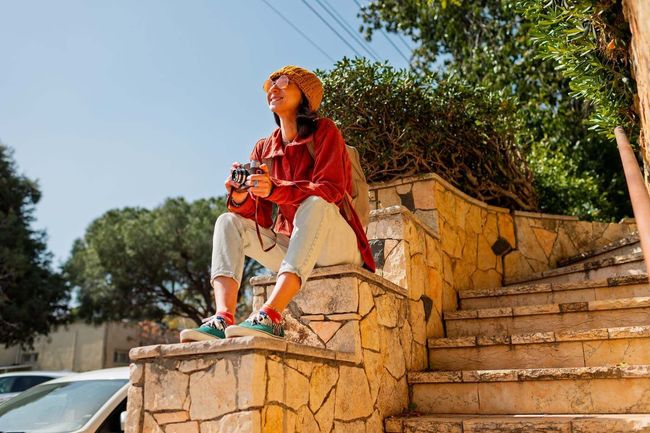 Una persona con camisa y sombrero rojos está sentada en escalones de piedra al aire libre.