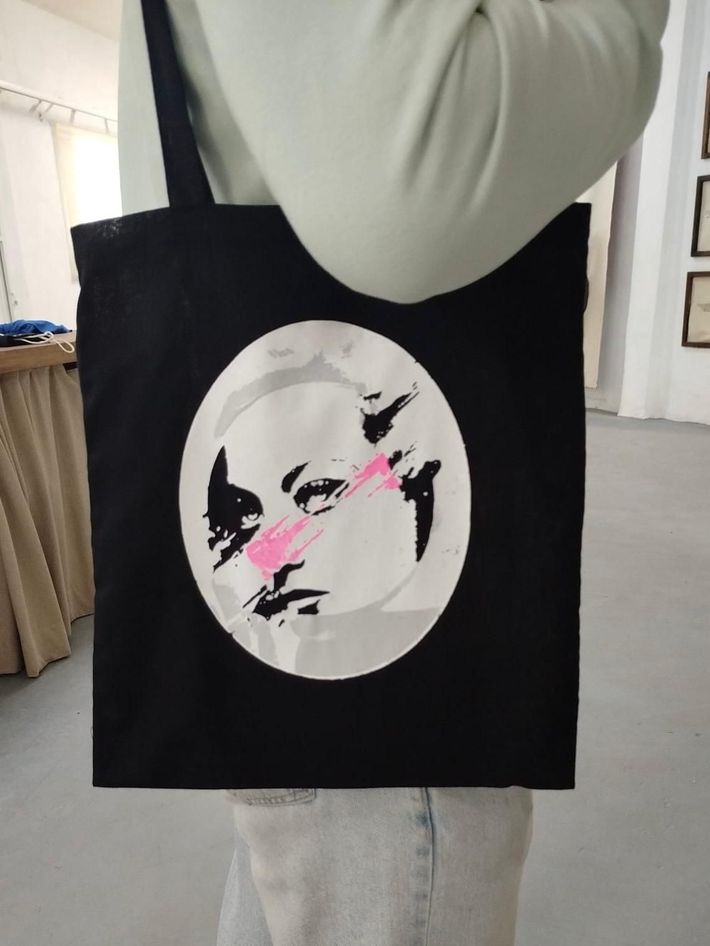Bolso de mano negro con un retrato estilizado en blanco y negro.