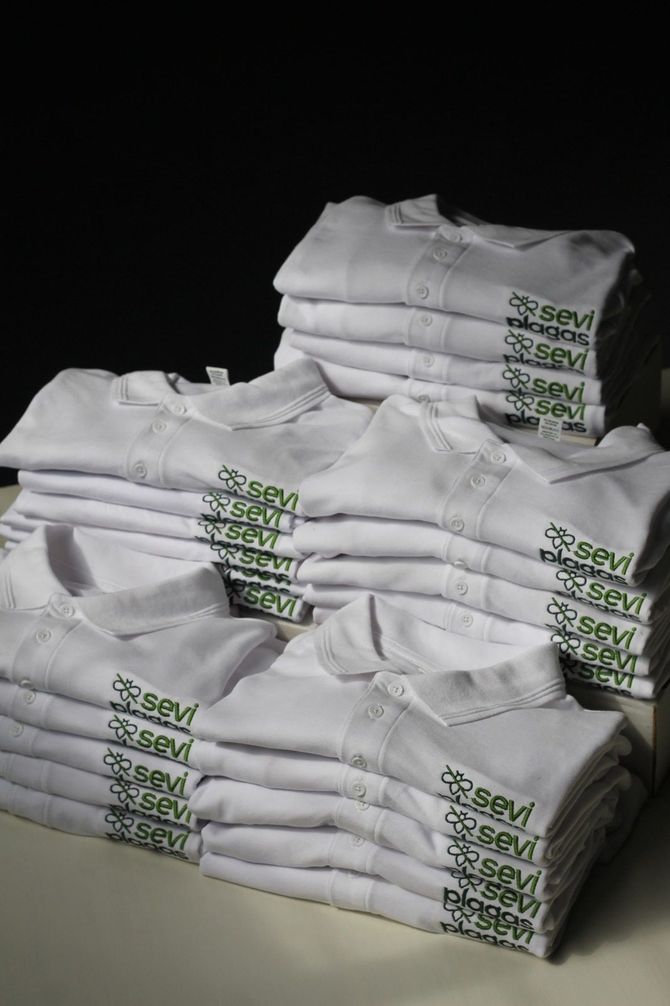 Camisetas blancas dobladas apiladas con etiquetas verdes impresas sobre un fondo oscuro.