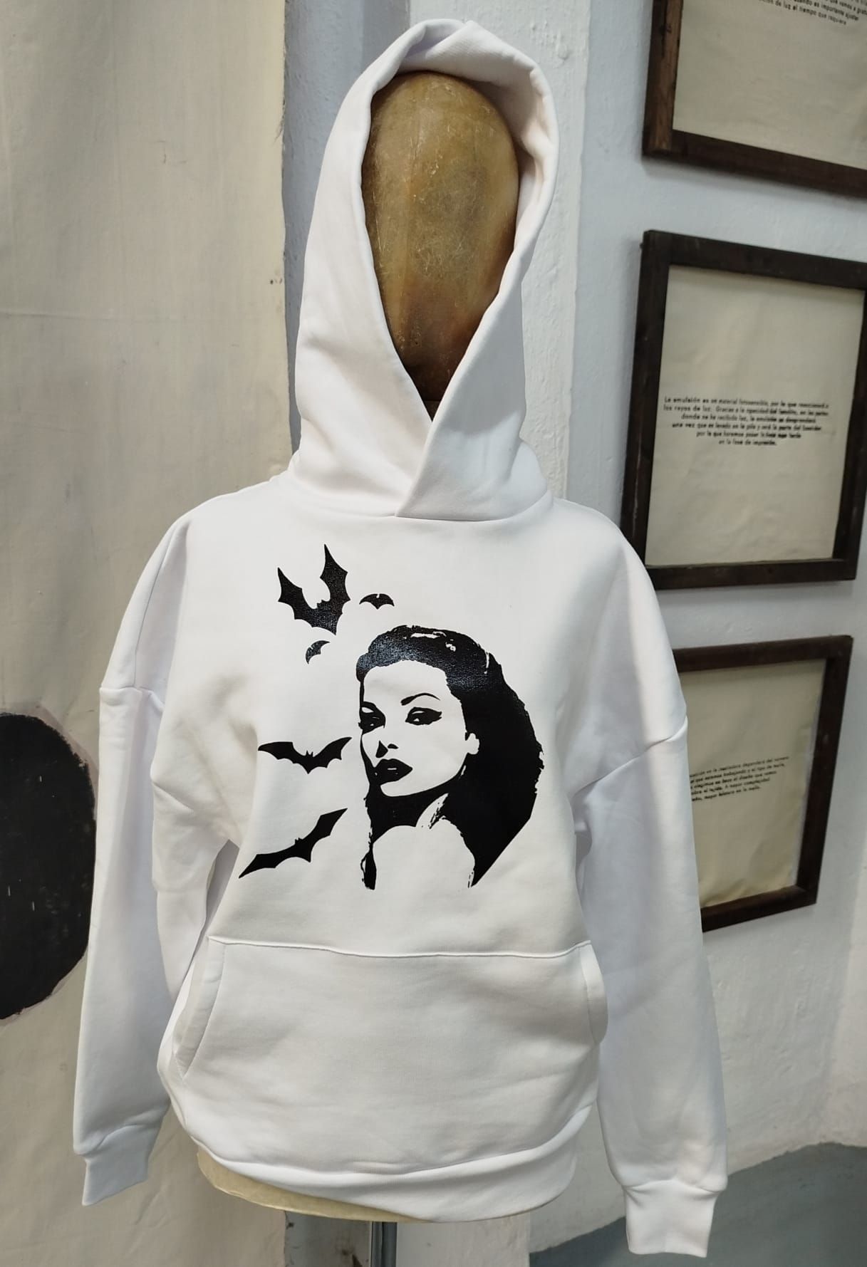 Sudadera blanca con capucha y estampado gráfico negro, expuesta en un maniquí en el interior.