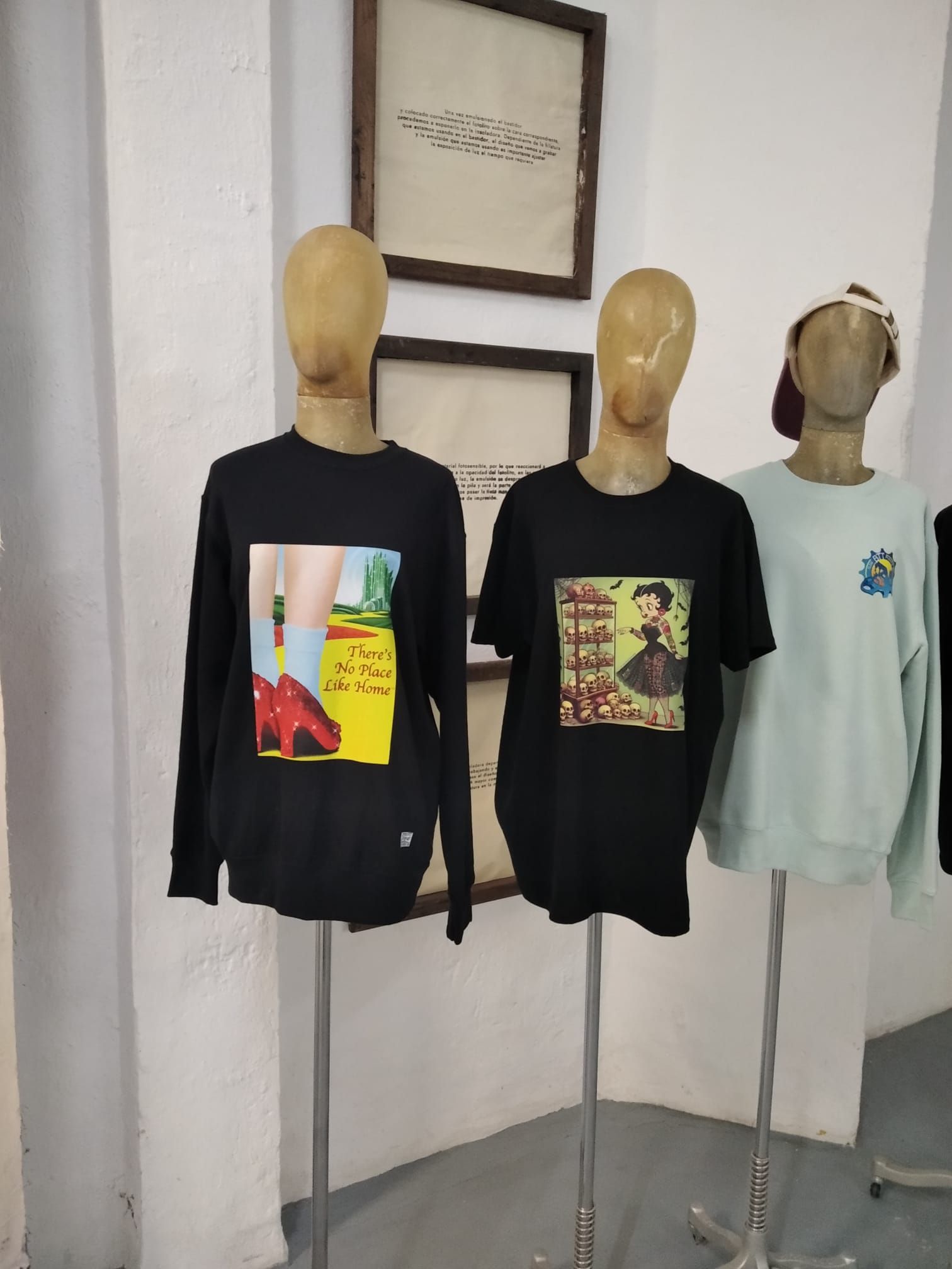 Tres maniquíes con camisetas gráficas de manga larga en negro y menta en un escaparate de ropa.