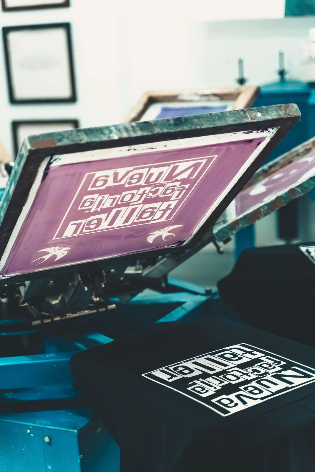 Montaje de serigrafía con camisetas rosas y un diseño impreso sobre una mesa de prensa en un taller.