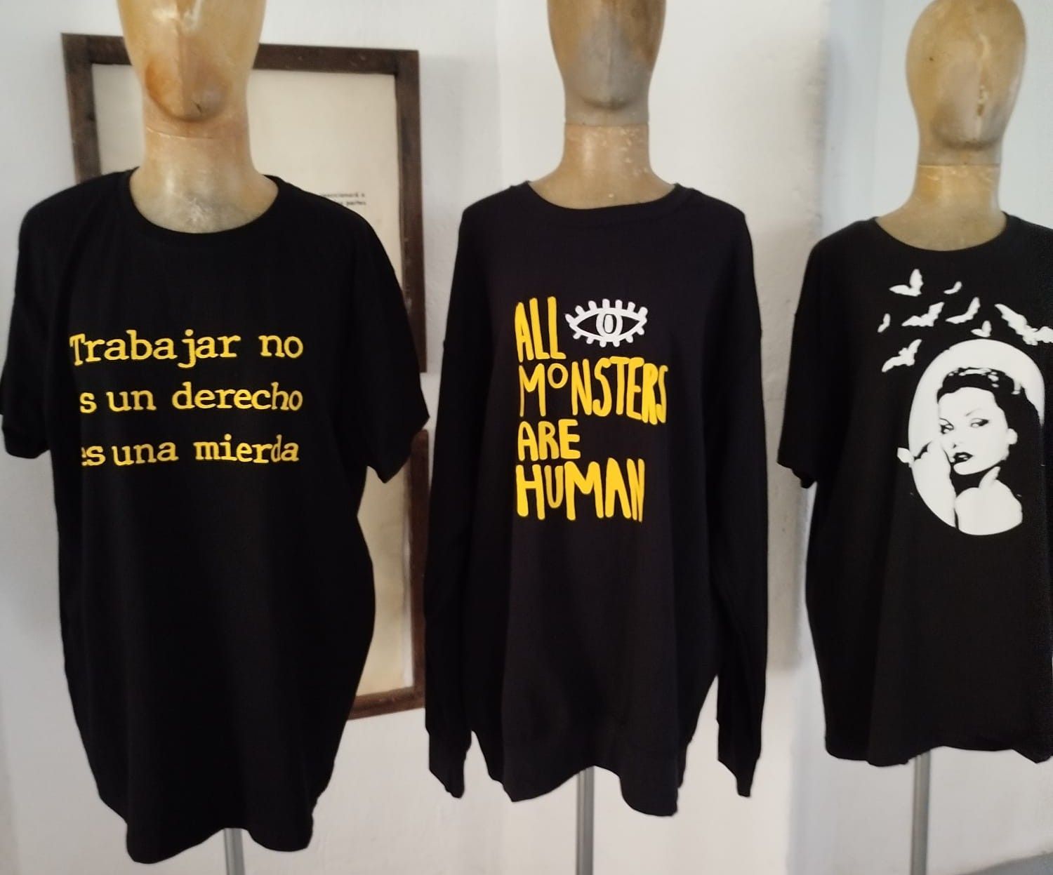 Tres camisas negras de manga larga sobre maniquíes con diseños gráficos de texto en amarillo y blanco.