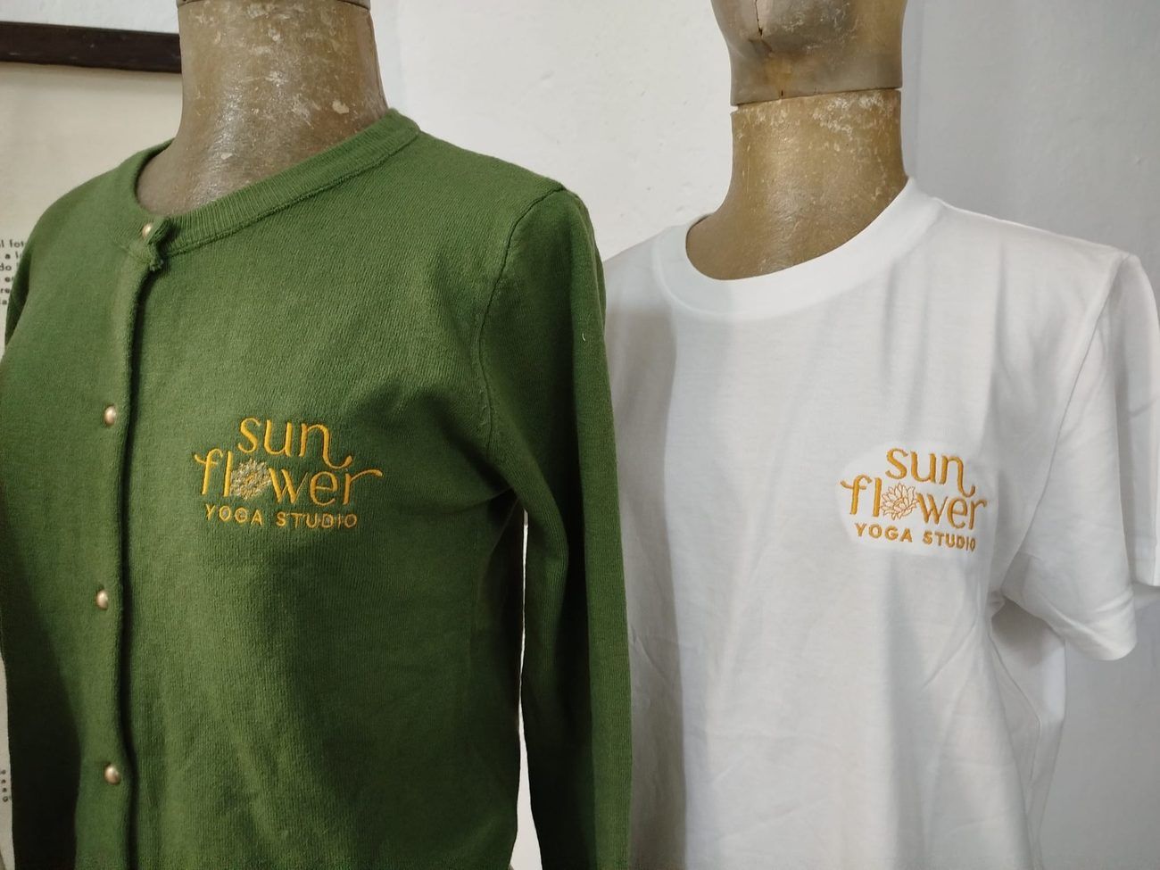 Dos maniquíes con camisetas de manga larga: una verde con logo dorado y otra blanca con logo dorado.