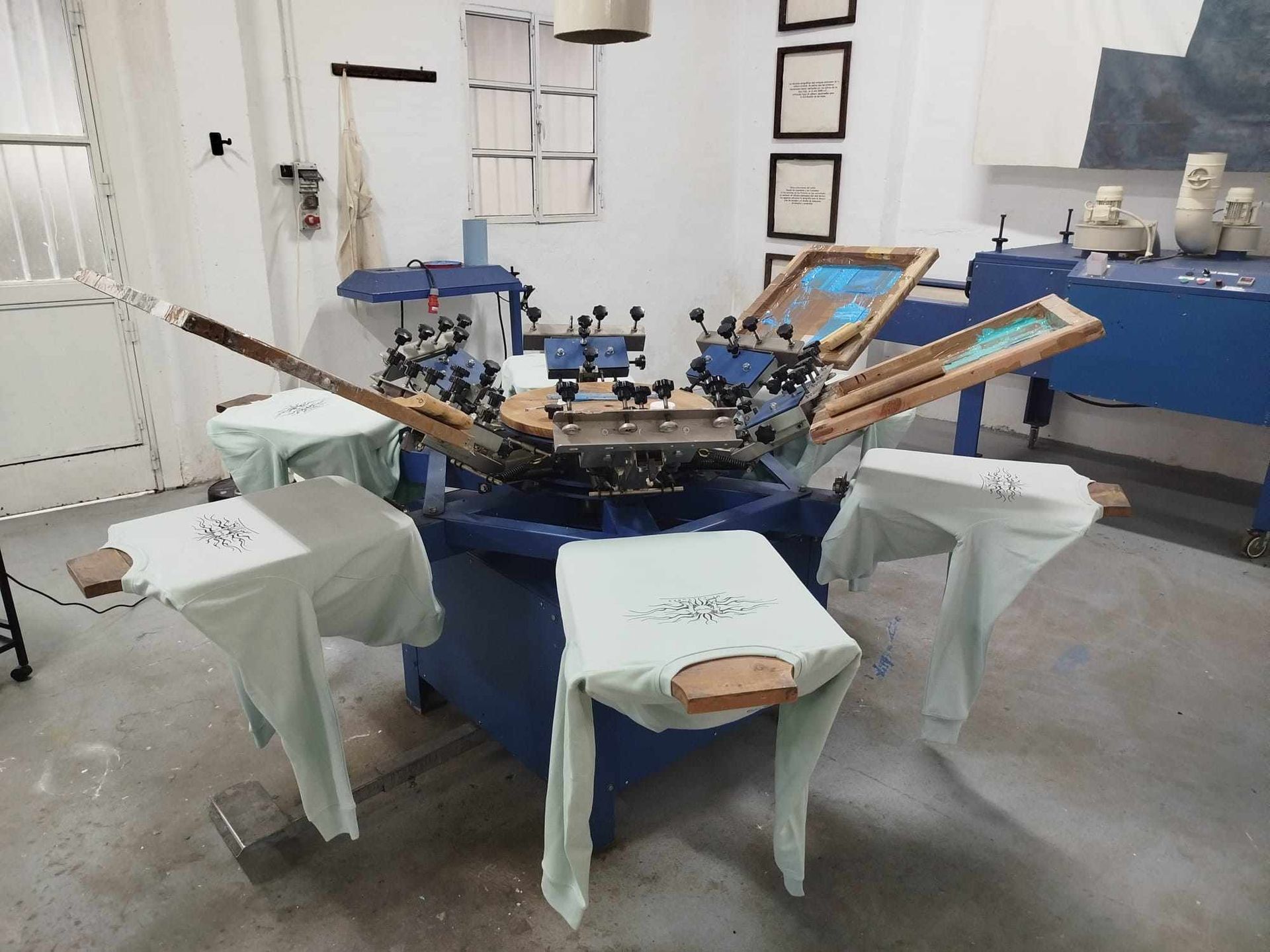 Taller industrial con una máquina azul rodeada de taburetes tapizados y herramientas en una habitación blanca.