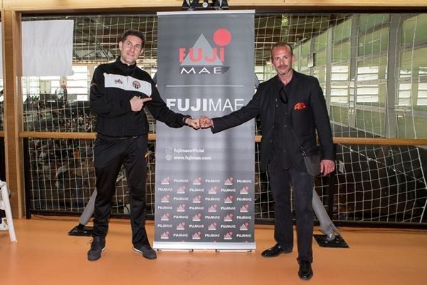 Dos hombres se dan la mano frente a un cartel de Fujimar