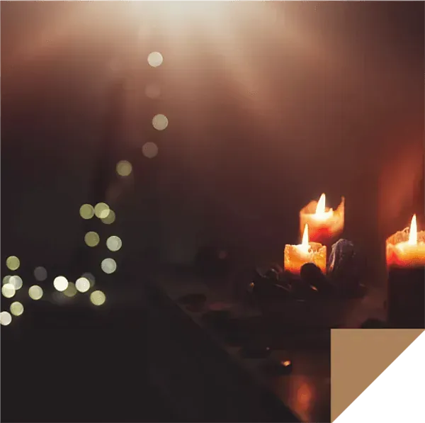 Tres velas encendidas sobre una mesa con un árbol de Navidad al fondo.