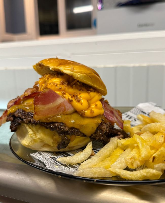 Hamburguesa doble con queso, tocino y papas fritas. La hamburguesa lleva pan dorado, queso derretido y tocino crujiente.