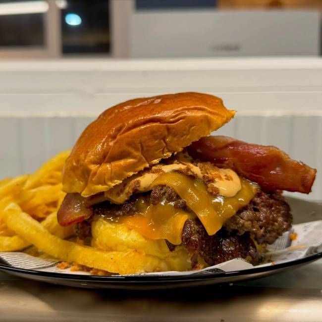 Hamburguesa doble con queso, tocino y papas fritas. La hamburguesa lleva pan dorado, queso derretido y tocino crujiente.