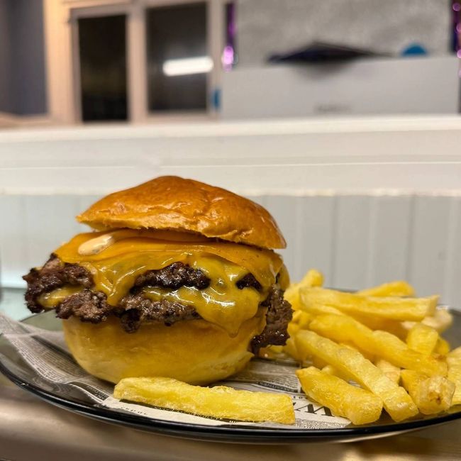 Hamburguesa doble con queso, tocino y papas fritas. La hamburguesa lleva pan dorado, queso derretido y tocino crujiente.