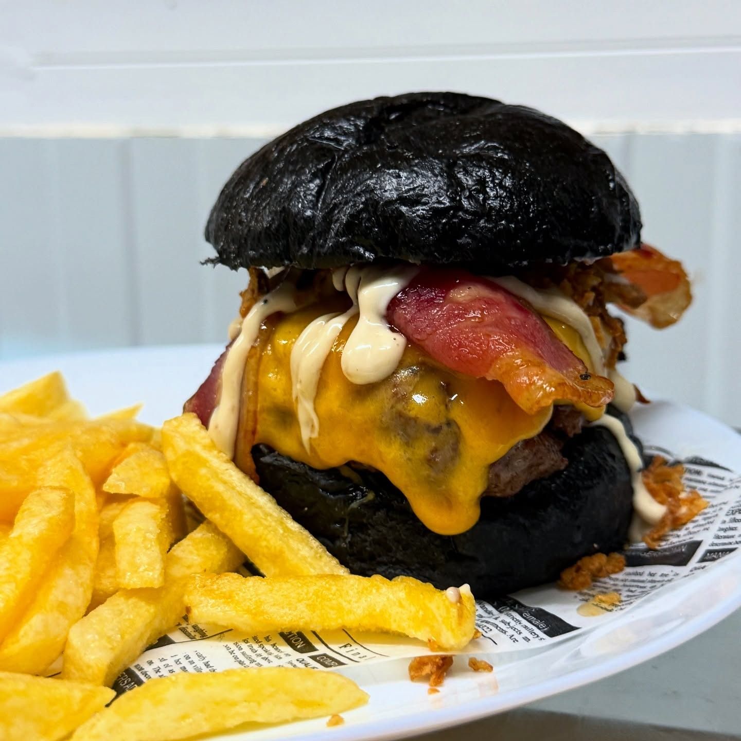 Hamburguesa de pan negro con queso, tocino, salsa y papas fritas en un plato.