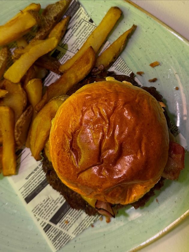 Una gran hamburguesa con queso, tocino y salsa, junto a una pila de papas fritas, en un plato.