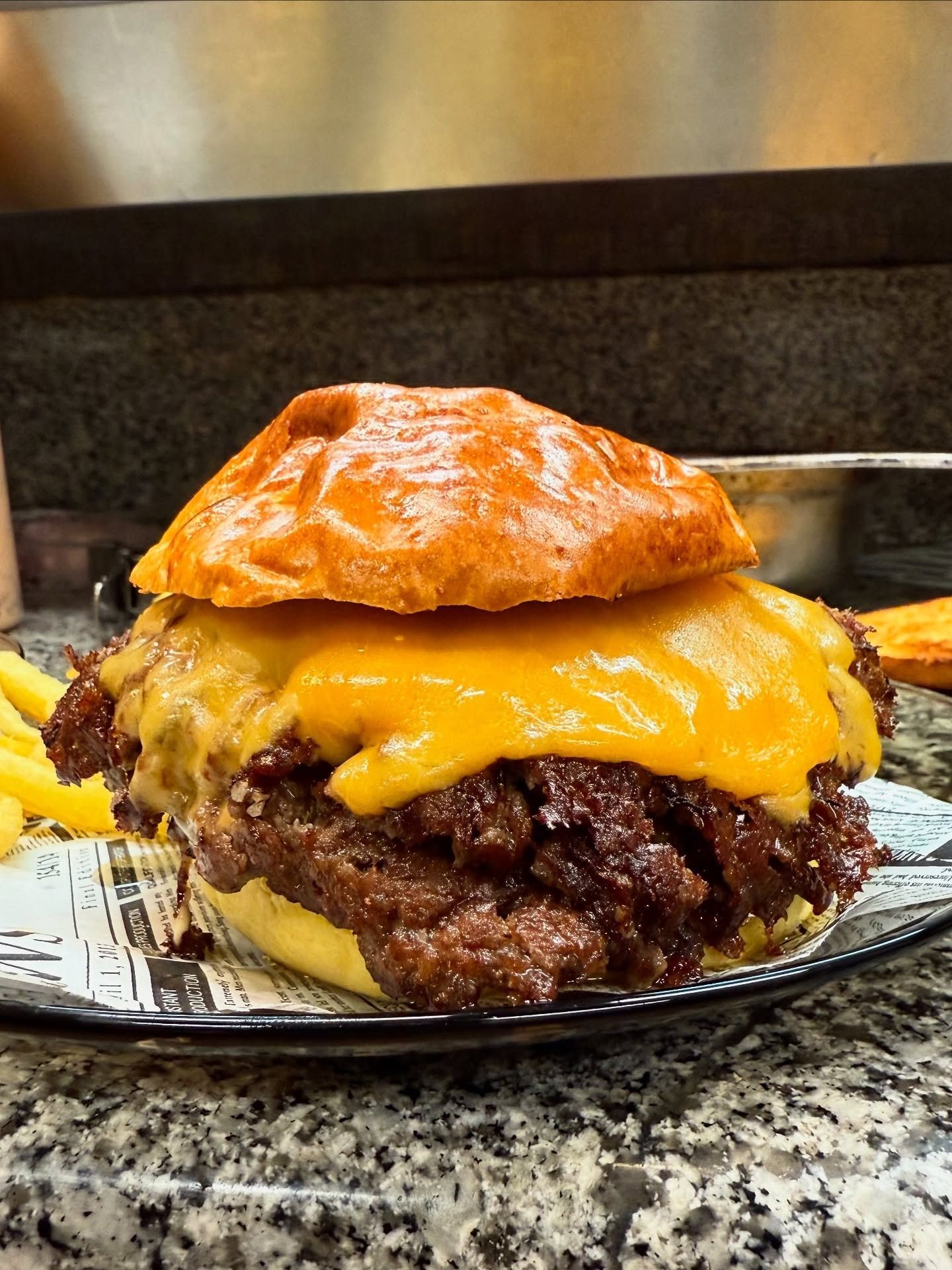 Una gran hamburguesa con queso, tocino y salsa, junto a una pila de papas fritas, en un plato.