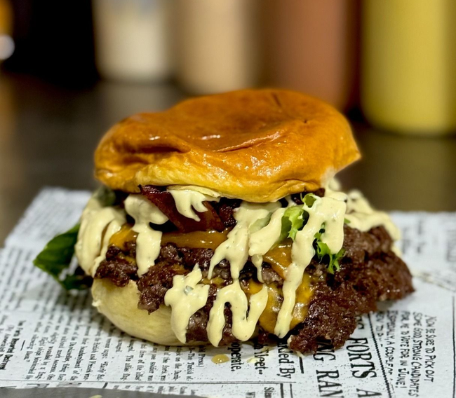 Hamburguesa doble con queso, tocino y papas fritas. La hamburguesa lleva pan dorado, queso derretido y tocino crujiente.