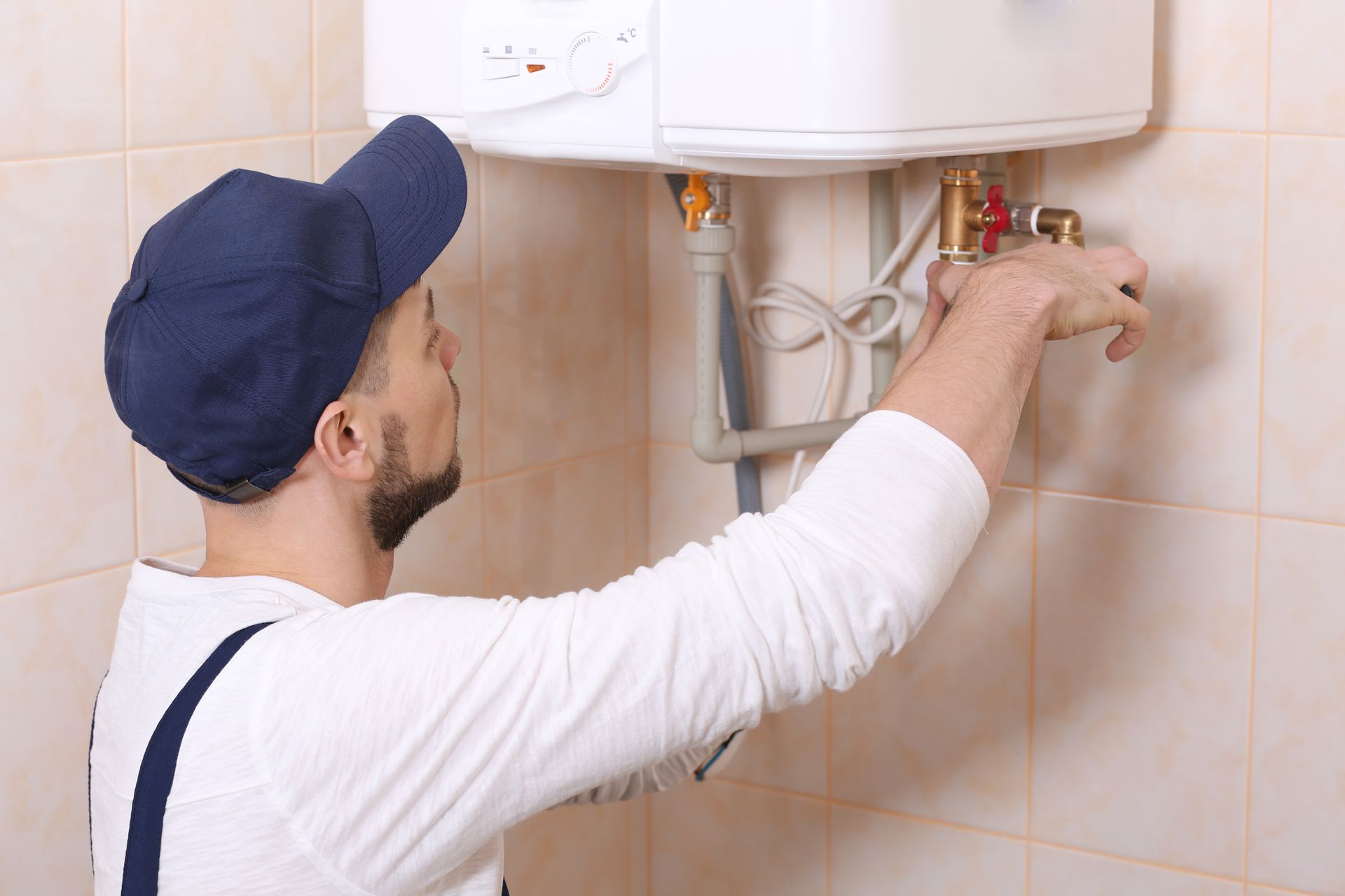 Un technicien ajuste les vannes d'un chauffe-eau mural dans une salle de bains carrelée.