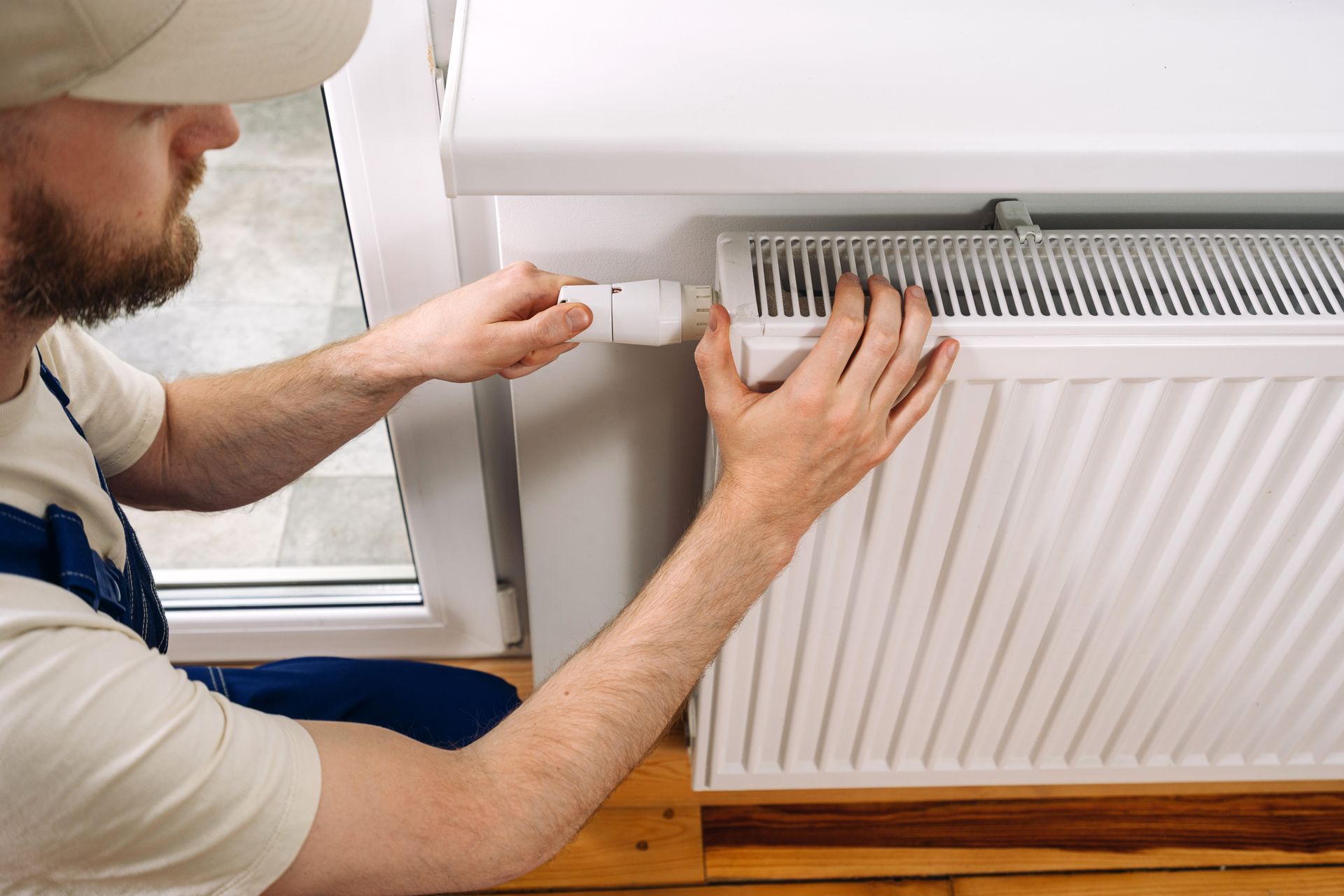 Un technicien nettoie un radiateur blanc avec une brosse près d'une fenêtre.