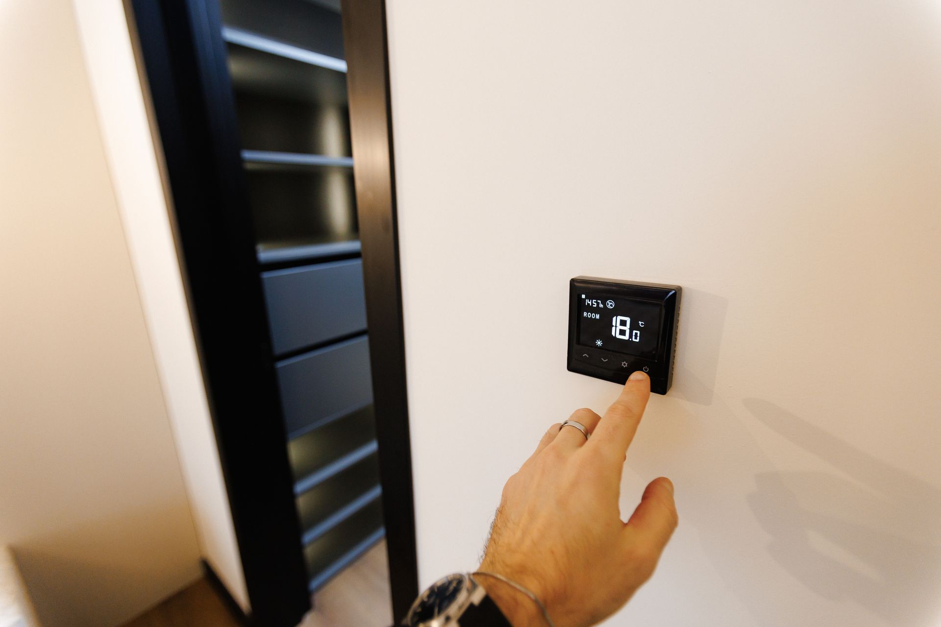 Réglage manuel d'un thermostat mural numérique près d'une porte dans une pièce beige.