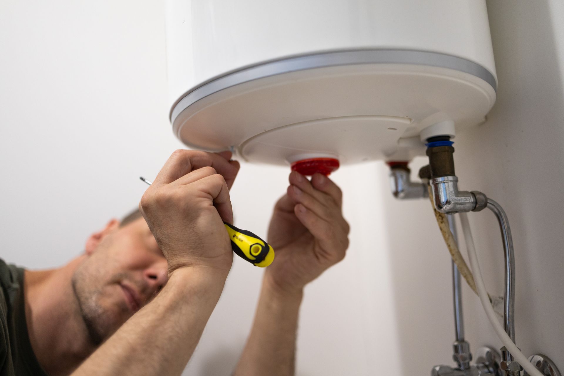 Un technicien répare un chauffe-eau sous un évier à l'aide d'une clé et d'un mètre ruban jaune.