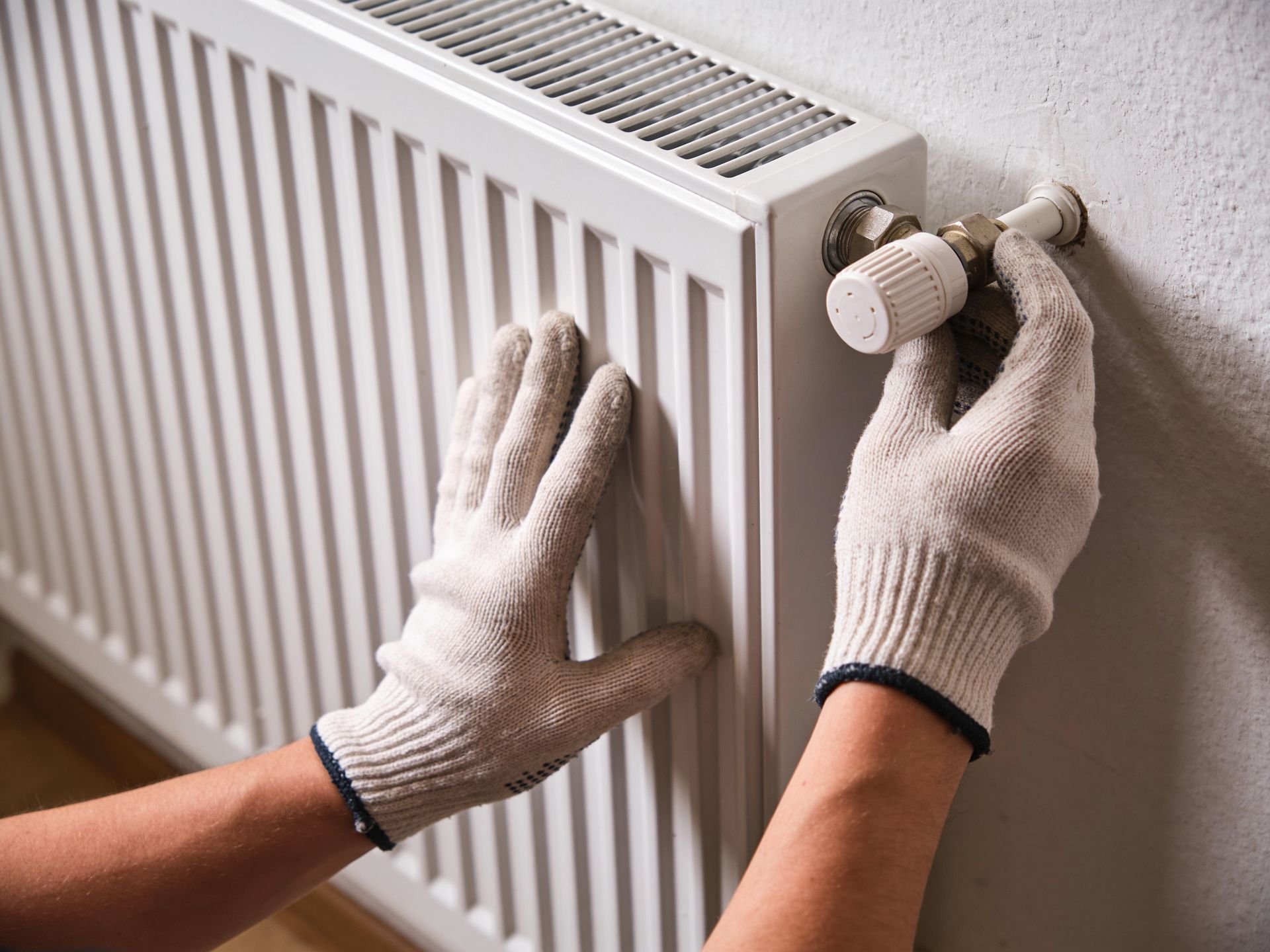 Des mains gantées règlent le thermostat blanc d'un radiateur mural.